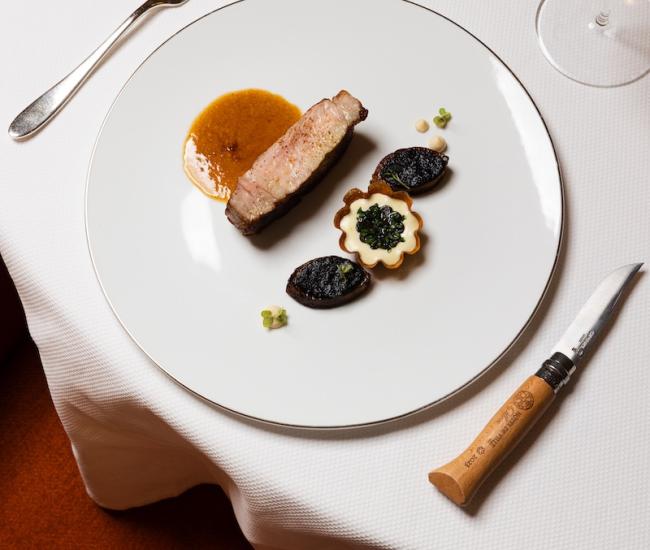 Table ronde dressée dans un restaurant gastronomique, avec assiettes blanches, verres, serviettes élégantes et bouquet de fleurs, dans une ambiance chaleureuse et raffinée.
