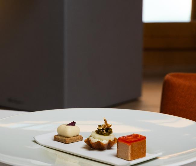 Table ronde dressée dans un restaurant gastronomique, avec assiettes blanches, verres, serviettes élégantes et bouquet de fleurs, dans une ambiance chaleureuse et raffinée.