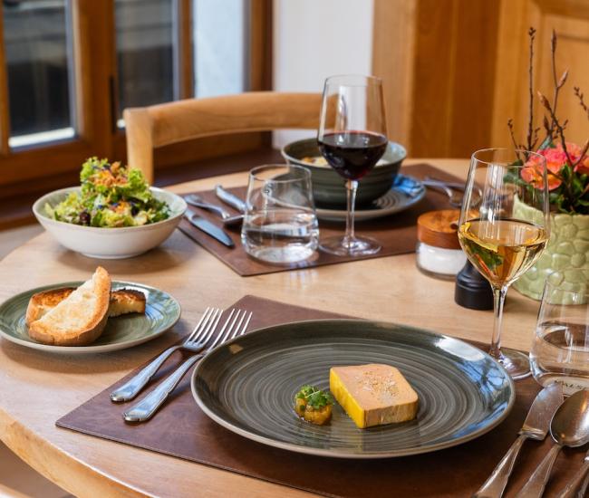 Table de Brasserie avec foie gras dressé, pain grillé, salade fraîche et verres de vin, dans une ambiance lumineuse et élégante.