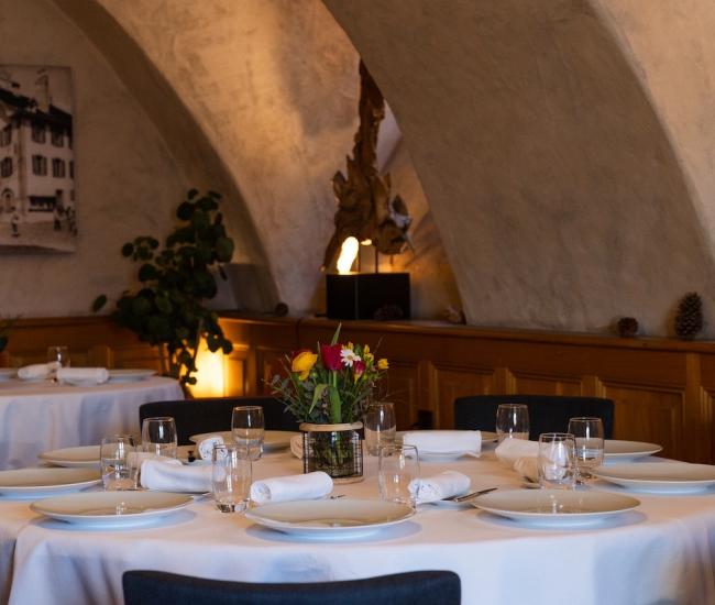 Table ronde dressée dans un restaurant gastronomique, avec assiettes blanches, verres, serviettes élégantes et bouquet de fleurs, dans une ambiance chaleureuse et raffinée, pour un groupe 